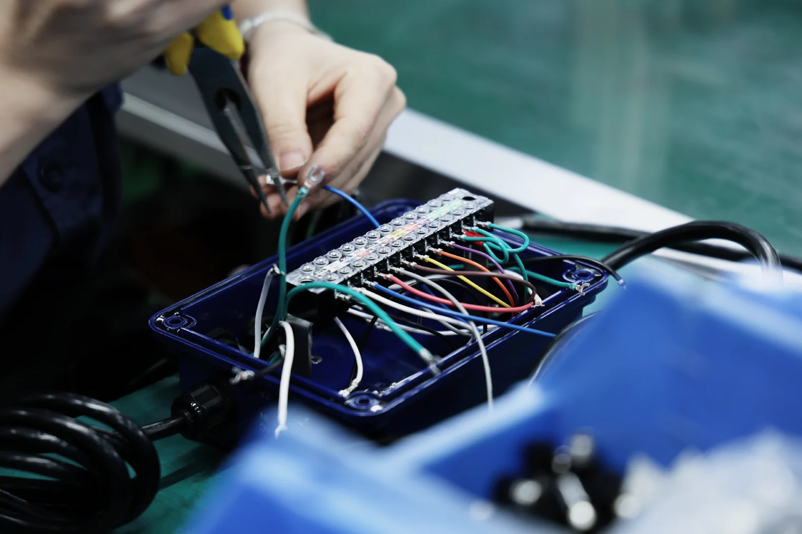 Operator terminating colour-coded wiring to a terminal block inside a sealed plastic enclosure during box build assembly