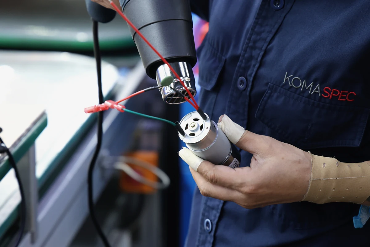 Technician holding a DC motor with crimped red and green harness leads for a fitness training machine