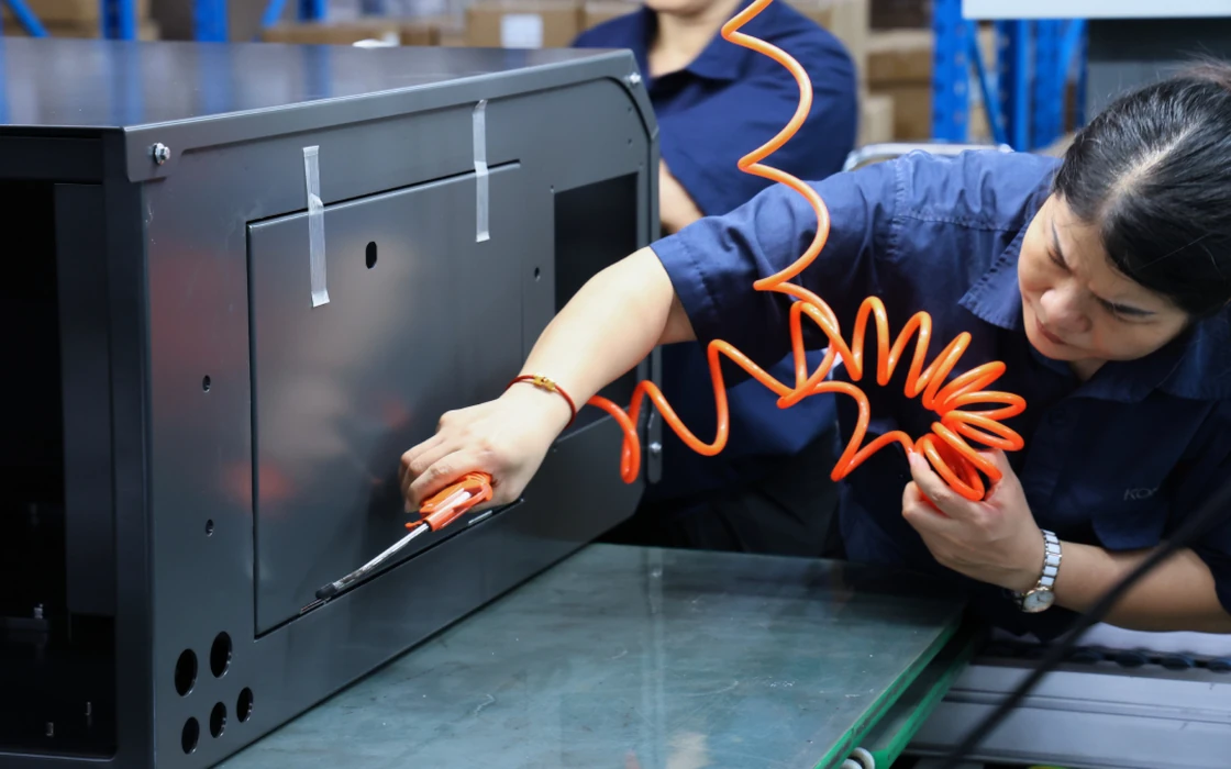 Technician fastening a metal enclosure with a pneumatic tool on the production floor
