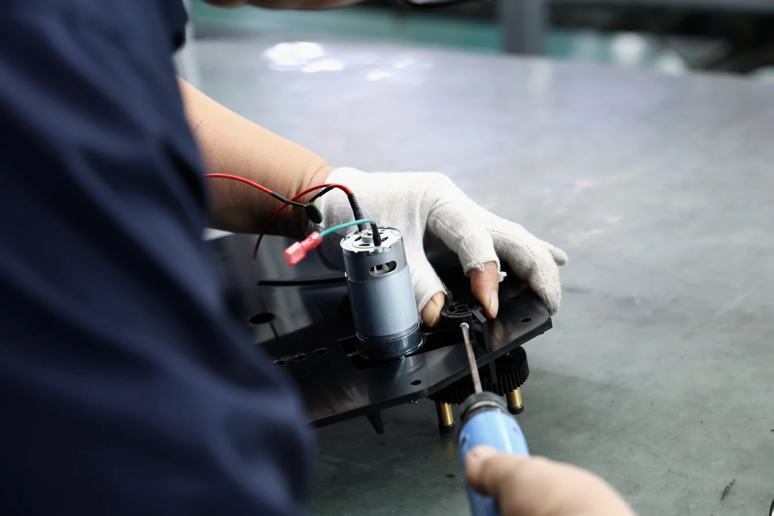 Operator fitting a motor and wiring into a moulded housing and driving a fastener at an assembly station