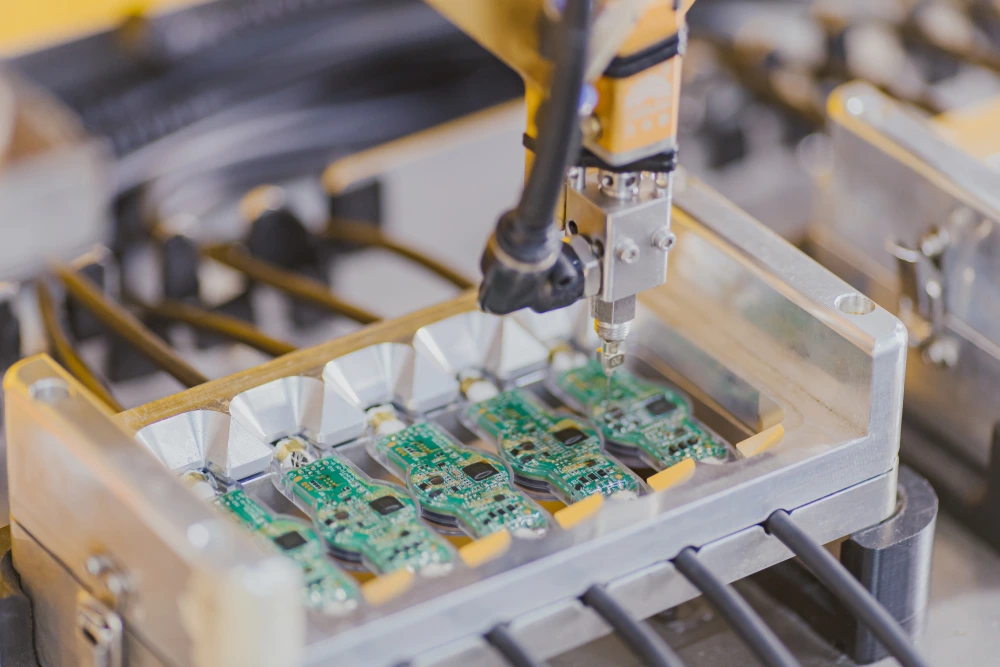 Automated dispensing head working across a row of populated PCBAs held in a machined aluminium fixture