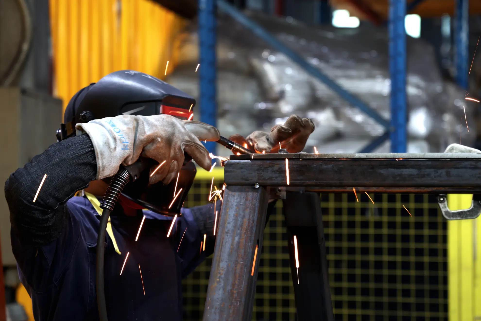 Welder in a protective helmet welding a steel tube frame, with sparks flying