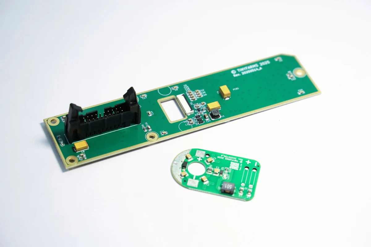Two populated PCB assemblies of different size and outline, a long narrow board and a small oval board, on a white surface