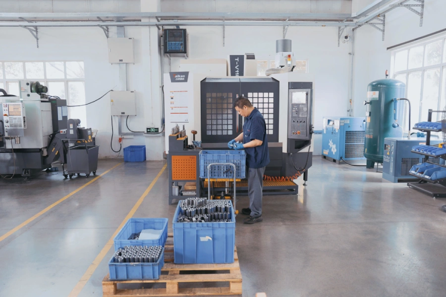 Crates of cylindrical metal parts staged next to a CNC mill
