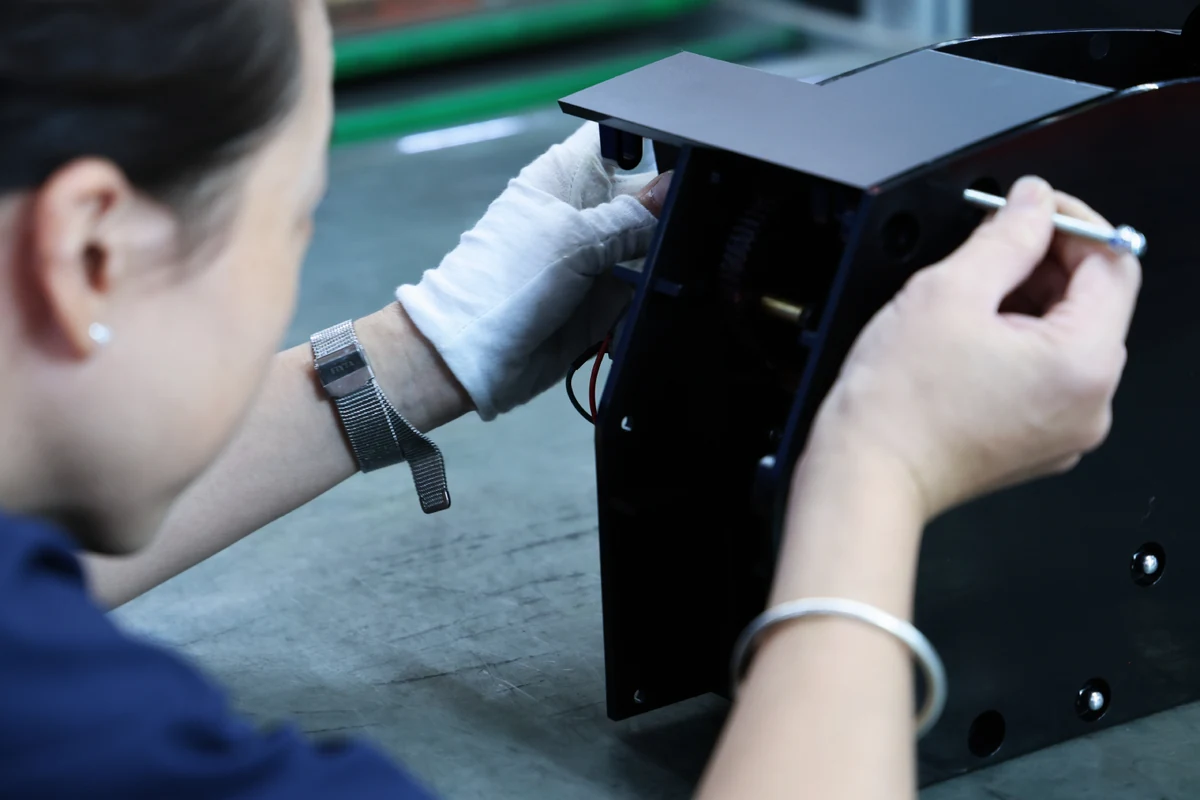 Assembler fitting internal components inside the black sheet metal housing of a tennis practice machine