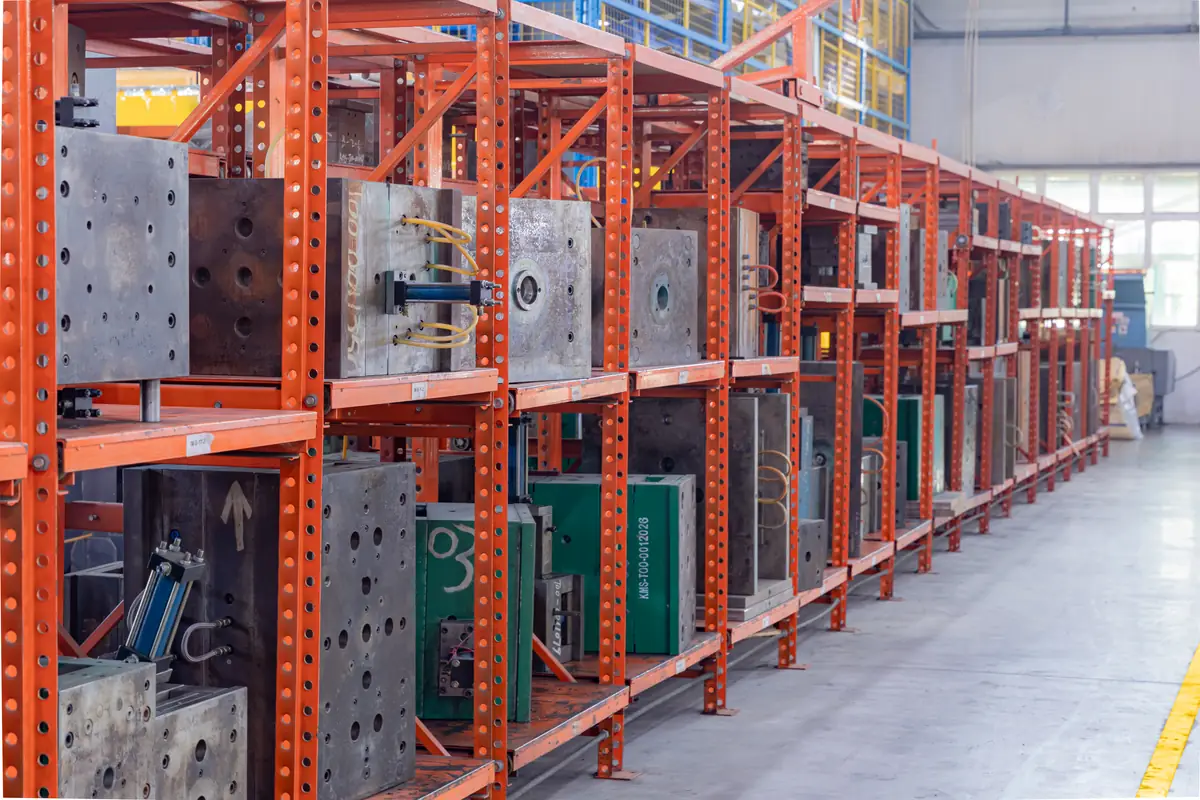 Injection mold tooling stored on steel racks, one tool tagged with a Komaspec (KMS) ID number