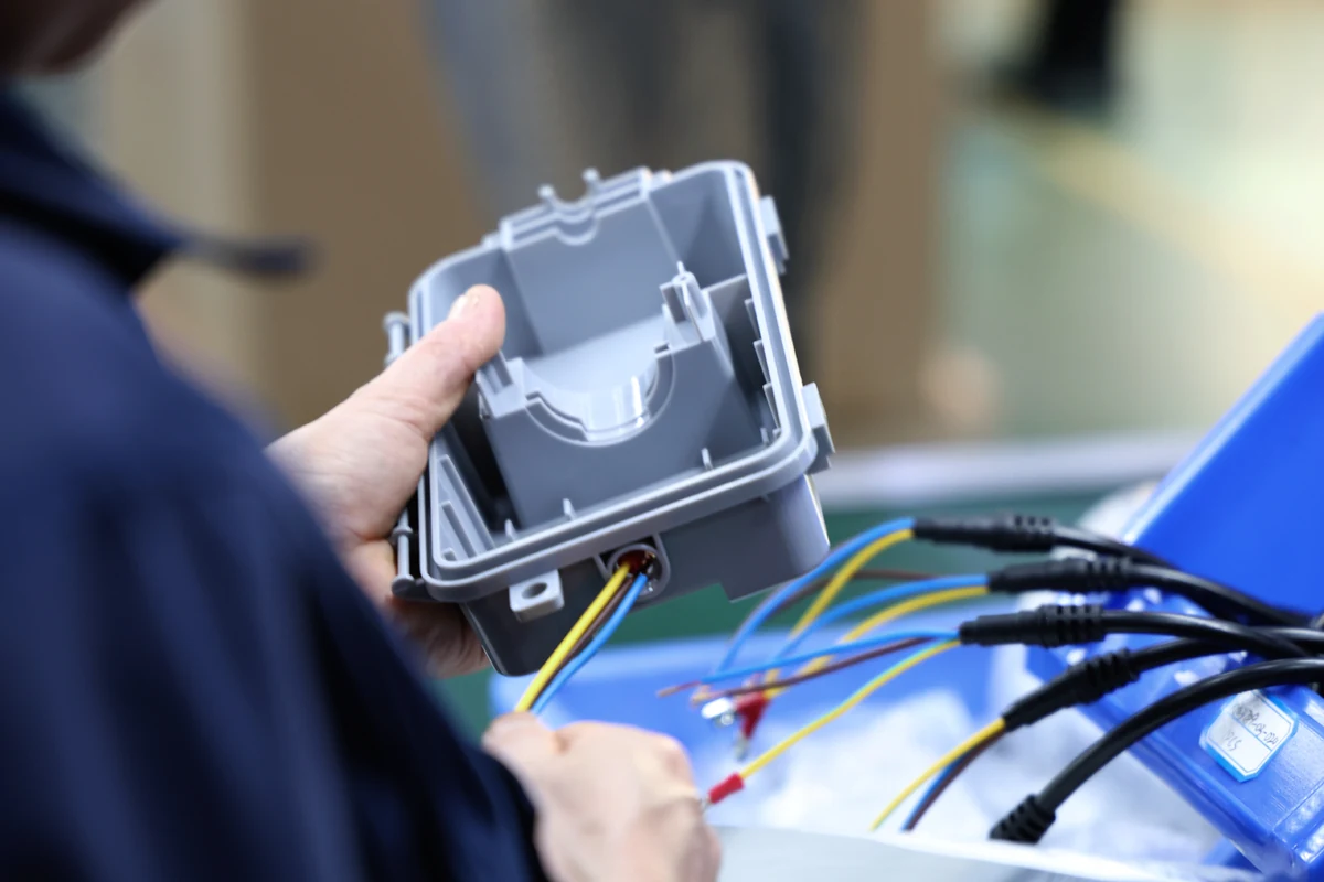 Operator routing a color-coded cable harness through the entry of an injection-molded plastic enclosure