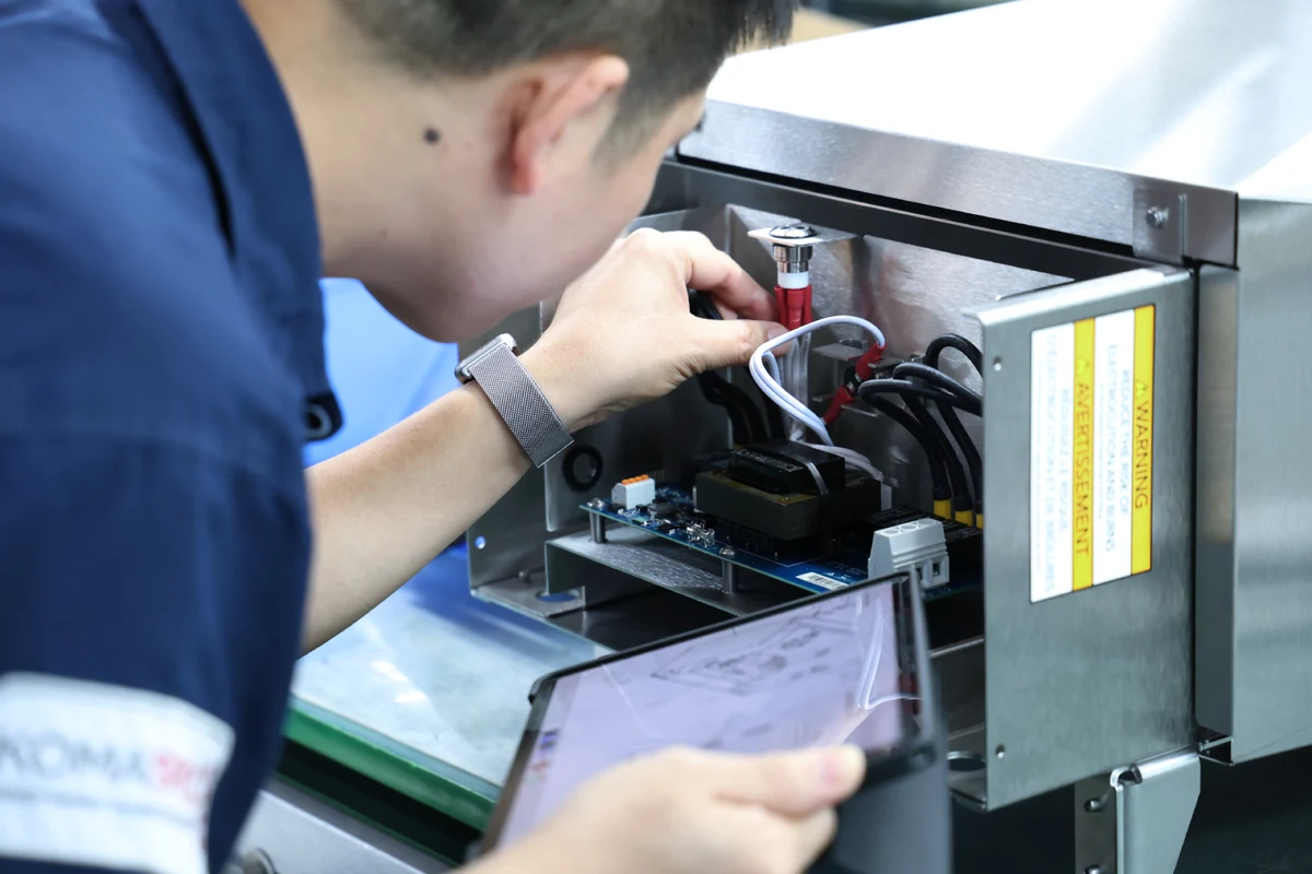 Technician wiring a PCBA inside a sheet metal box build enclosure while checking the assembly drawing on a tablet