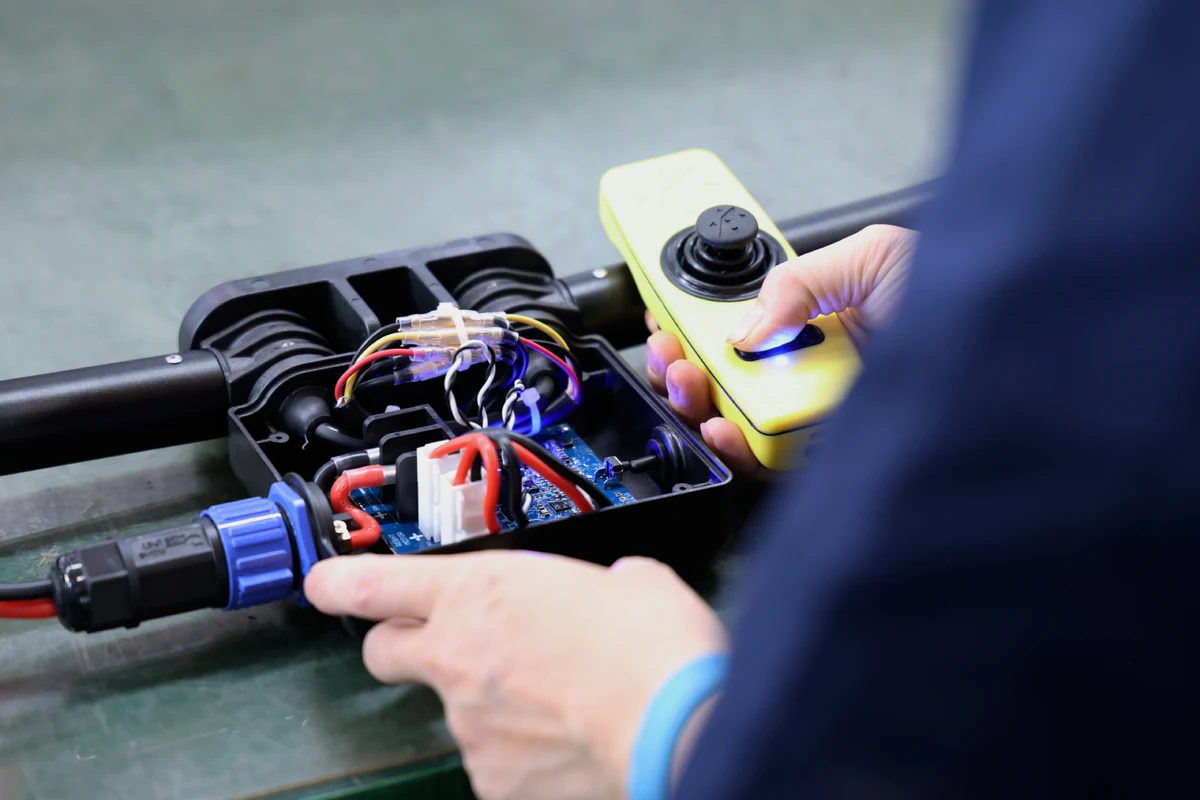 Operator assembling an electromechanical sub-assembly with an enclosure, internal PCB, wiring, connectors, and handheld control unit