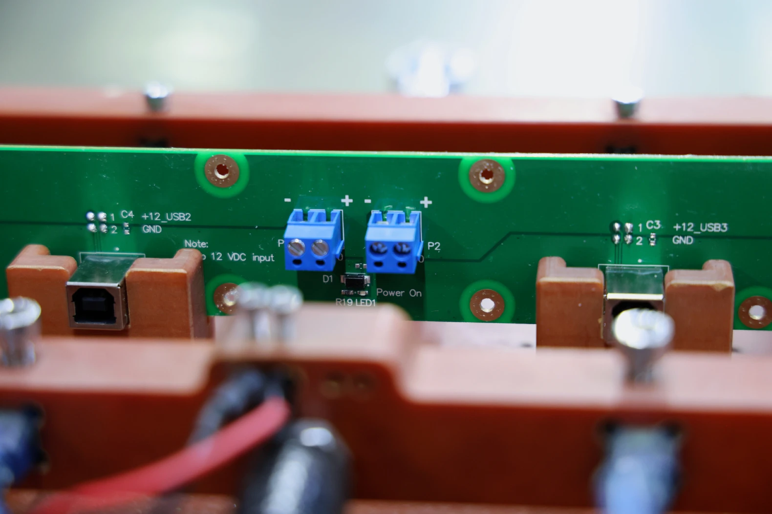 Populated PCB seated in a red test fixture, showing power terminal blocks, USB connectors and silkscreen labelling