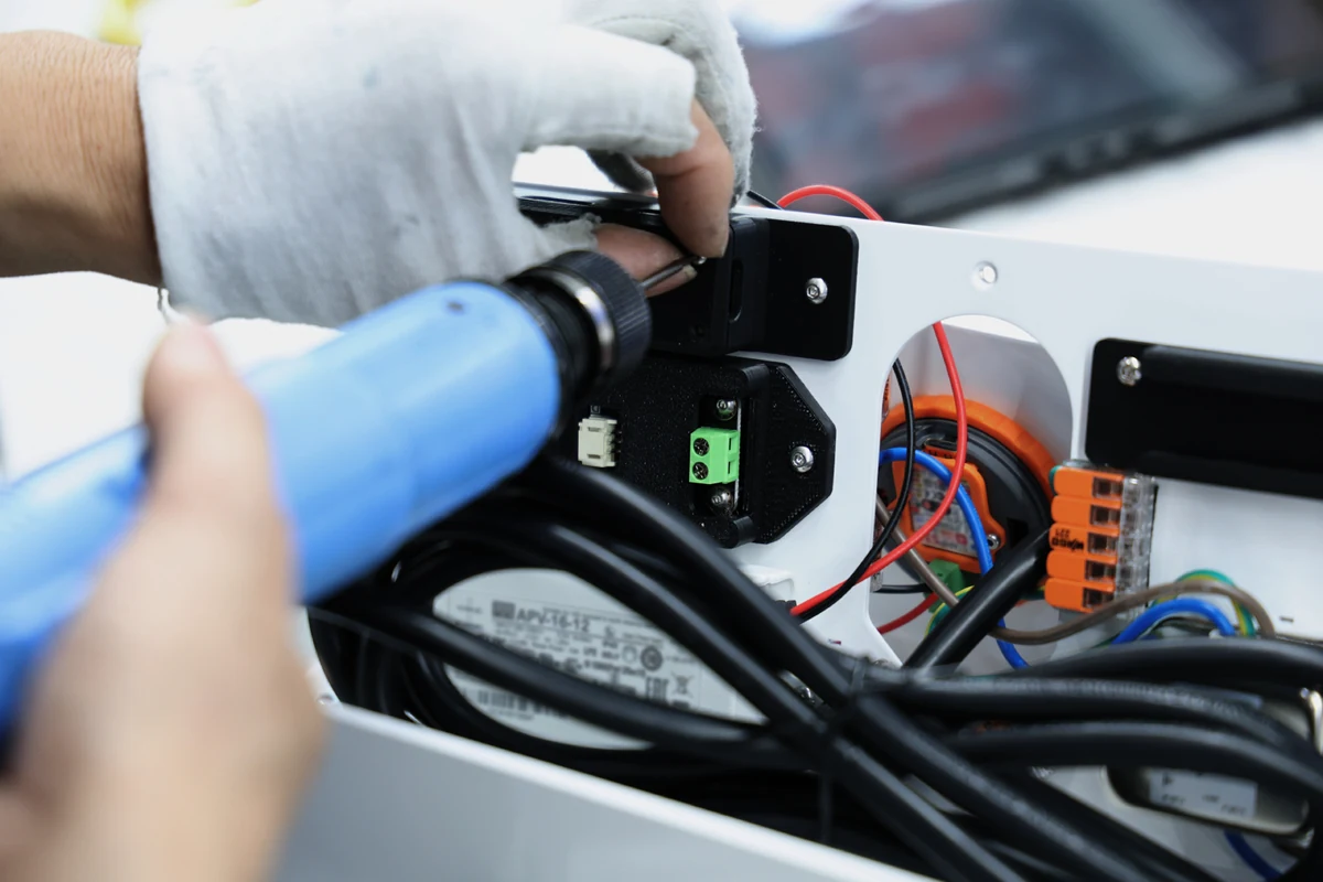 Technician fastening a panel-mount part on a sheet metal plate above a power supply and wiring harness