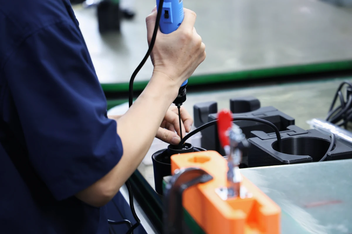 Operator using an electric screwdriver to assemble a sub-assembly module on a production workbench