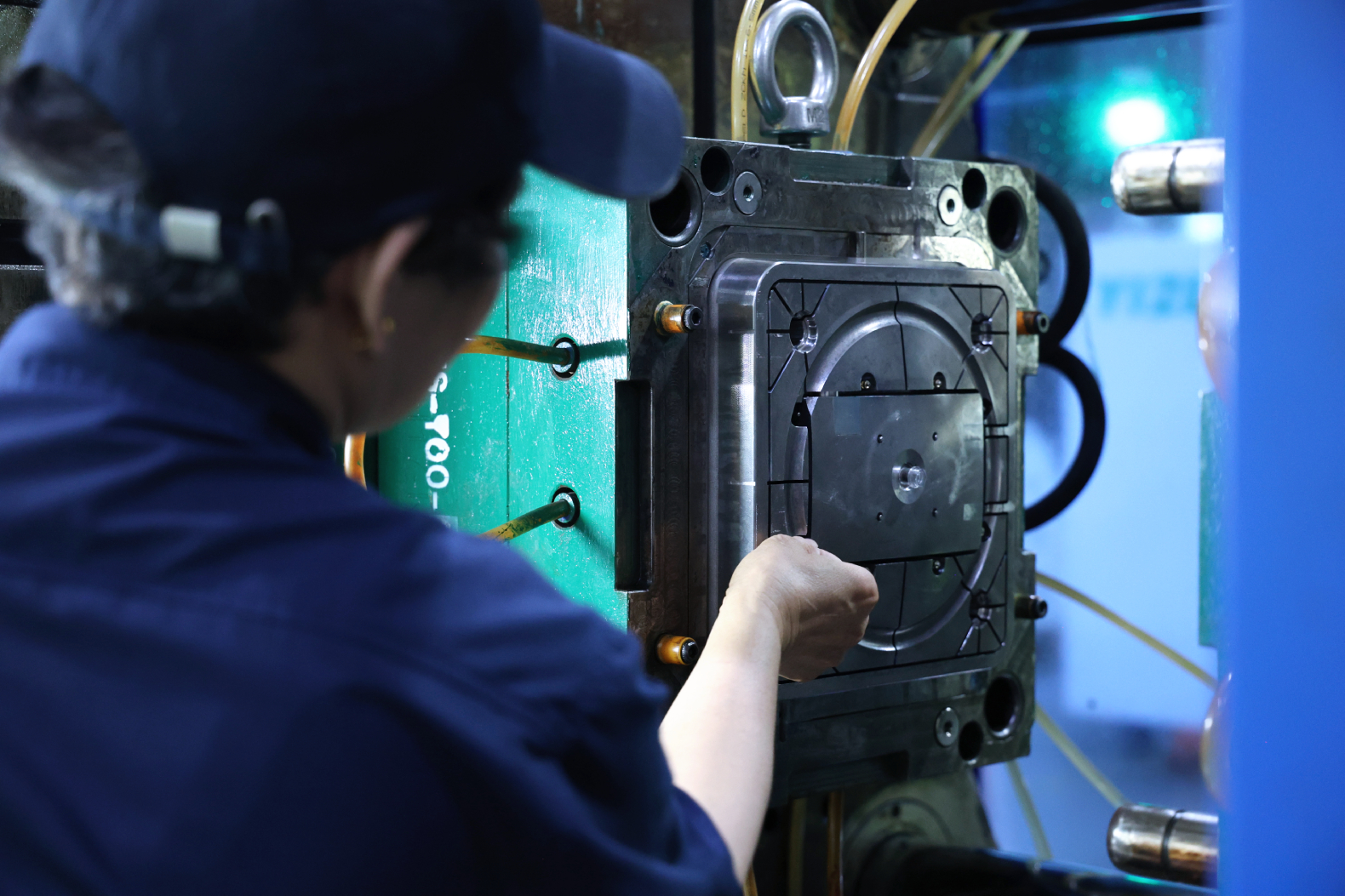Technician inspecting the exposed mold face of an injection mold mounted in an injection-molding machine.