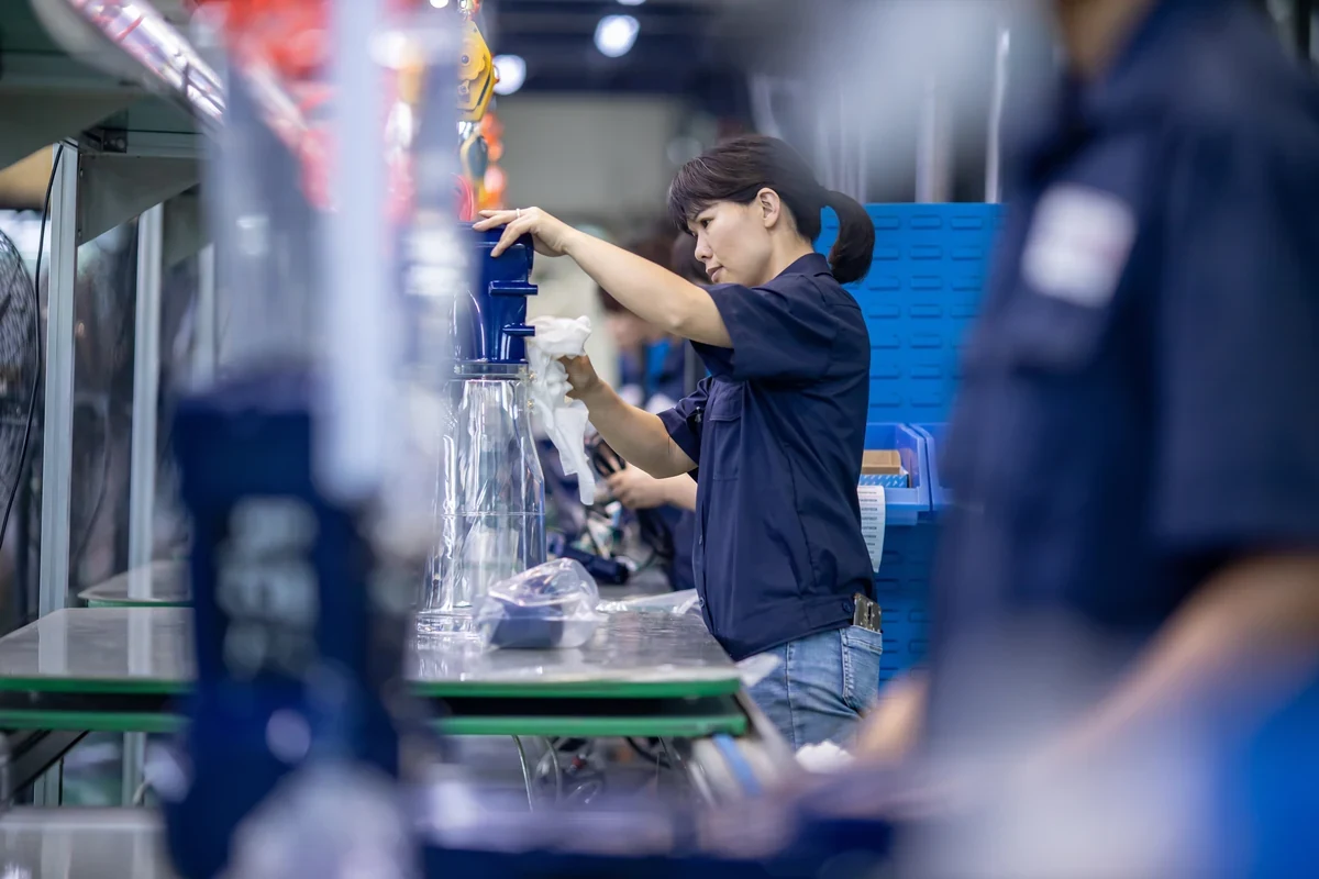 Worker at an assembly bench hand-finishing a molded blue plastic component with a cloth