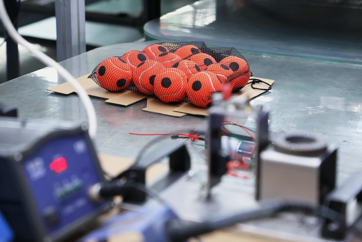 Practice tennis balls beside a motor drive assembly on a Komaspec fitness equipment production line